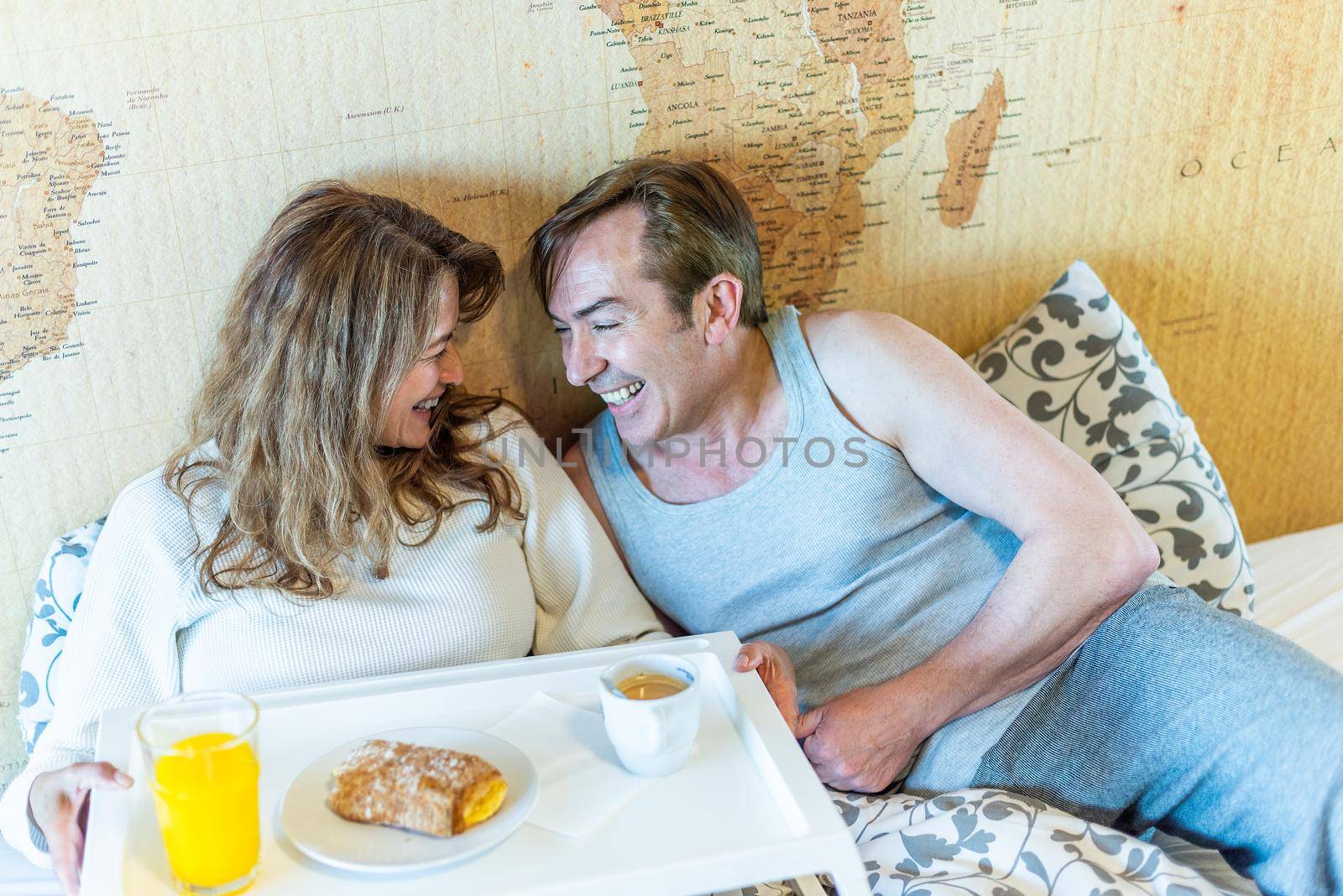 Mature couple laughing in bed, holding a tray with breakfast. High quality photo