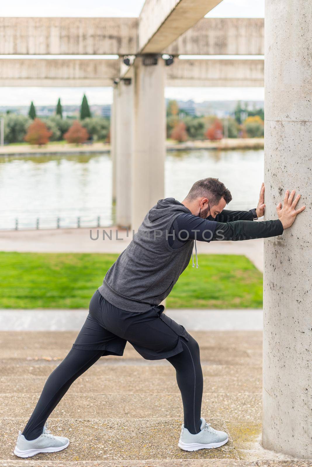 Runner with mask stretching in a park leaning against a wall. by ivanmoreno