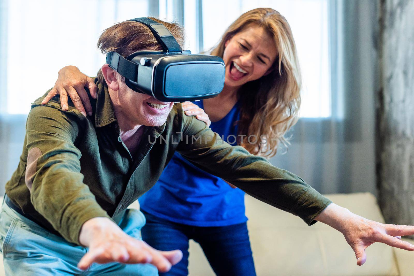 Mature married couple at home playing with virtual reality glasses. High quality photo