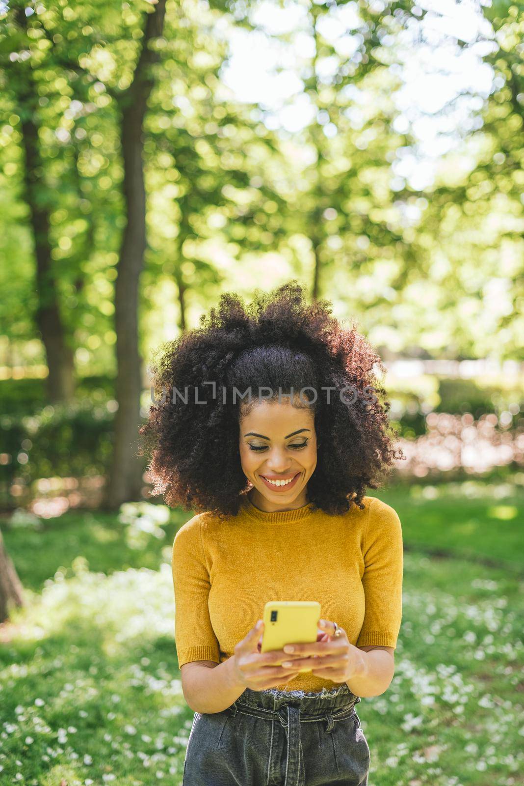 Pretty afro woman typing on mobile, in the forest. Selective focus.