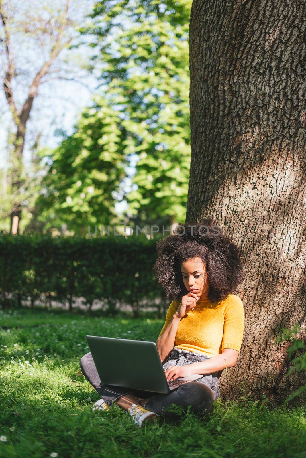 Beautiful afro woman typing on a laptop in a garden. Selective focus.