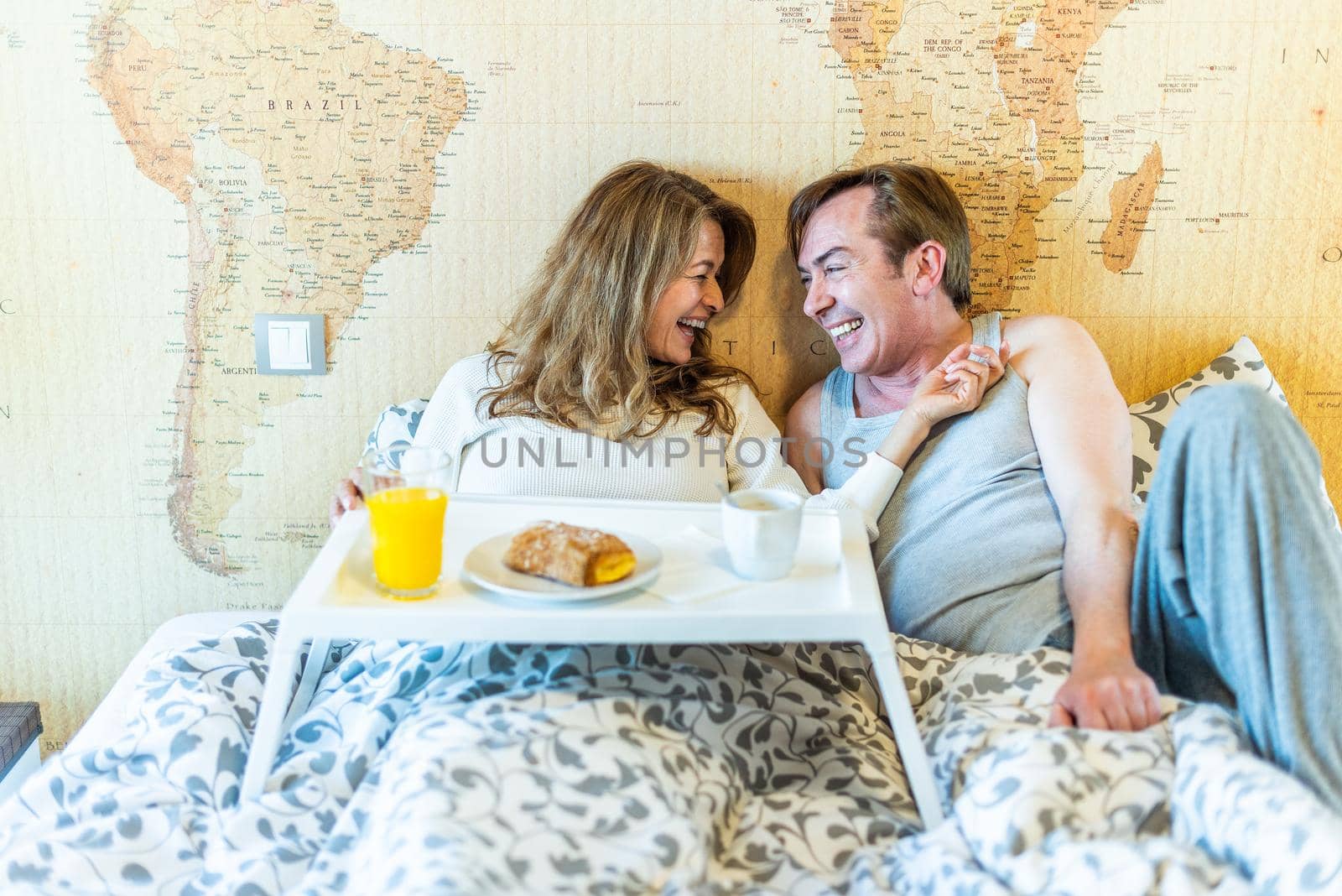 Mature couple laughing in bed, holding a tray with breakfast. High quality photo