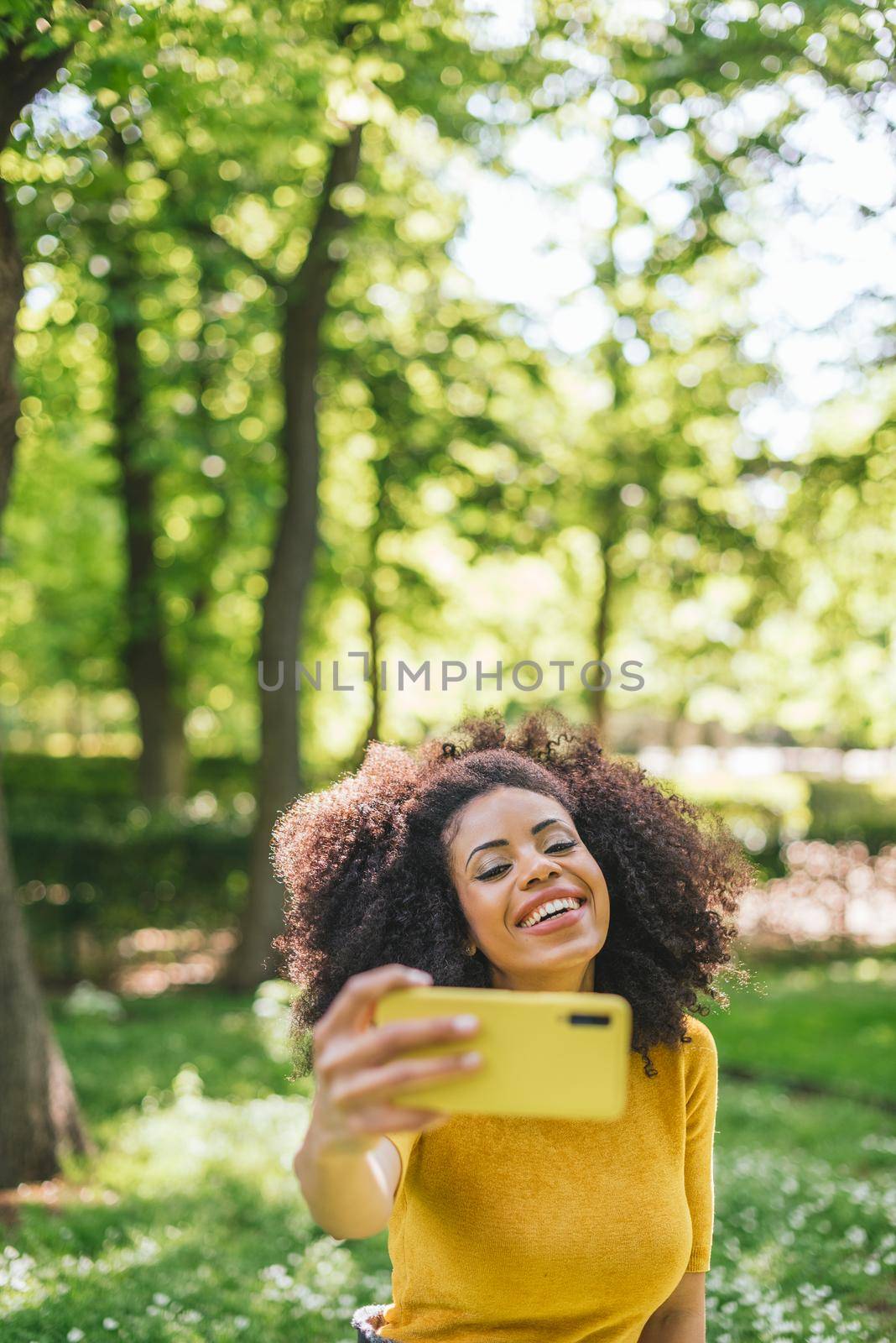 Pretty afro woman taking a selfie smiling in the forest. Selective focus.