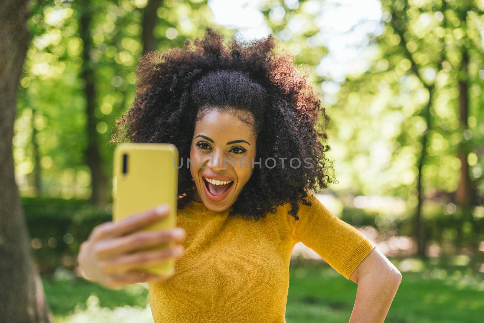 Pretty afro woman taking a selfie laughing in the forest. Selective focus.