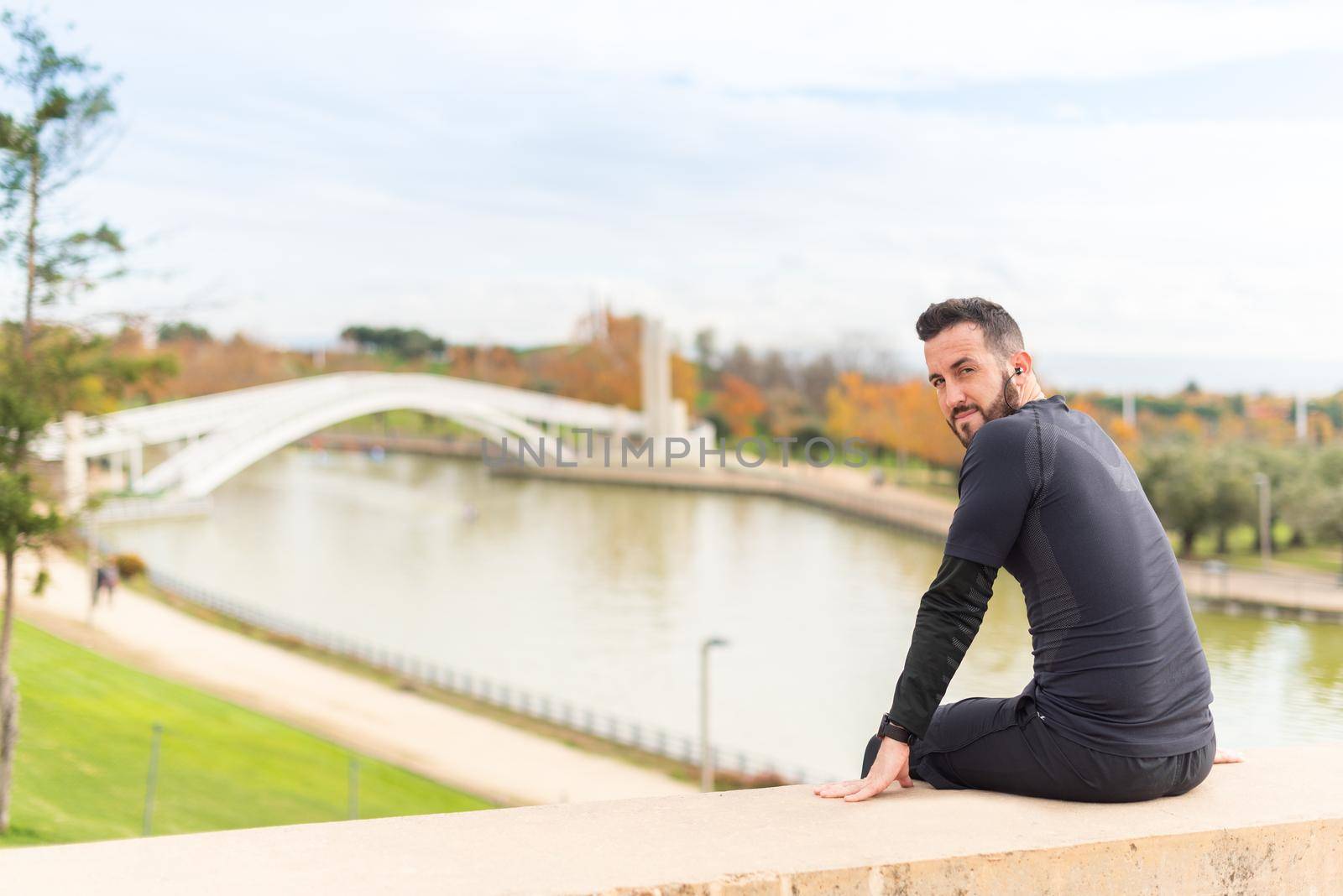 Sportsman with headphones sitting facing the camera in a park. High quality photo