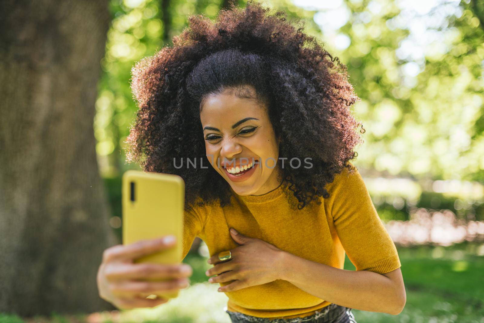 Pretty afro girl taking a selfie laughing in the forest. Selective focus.