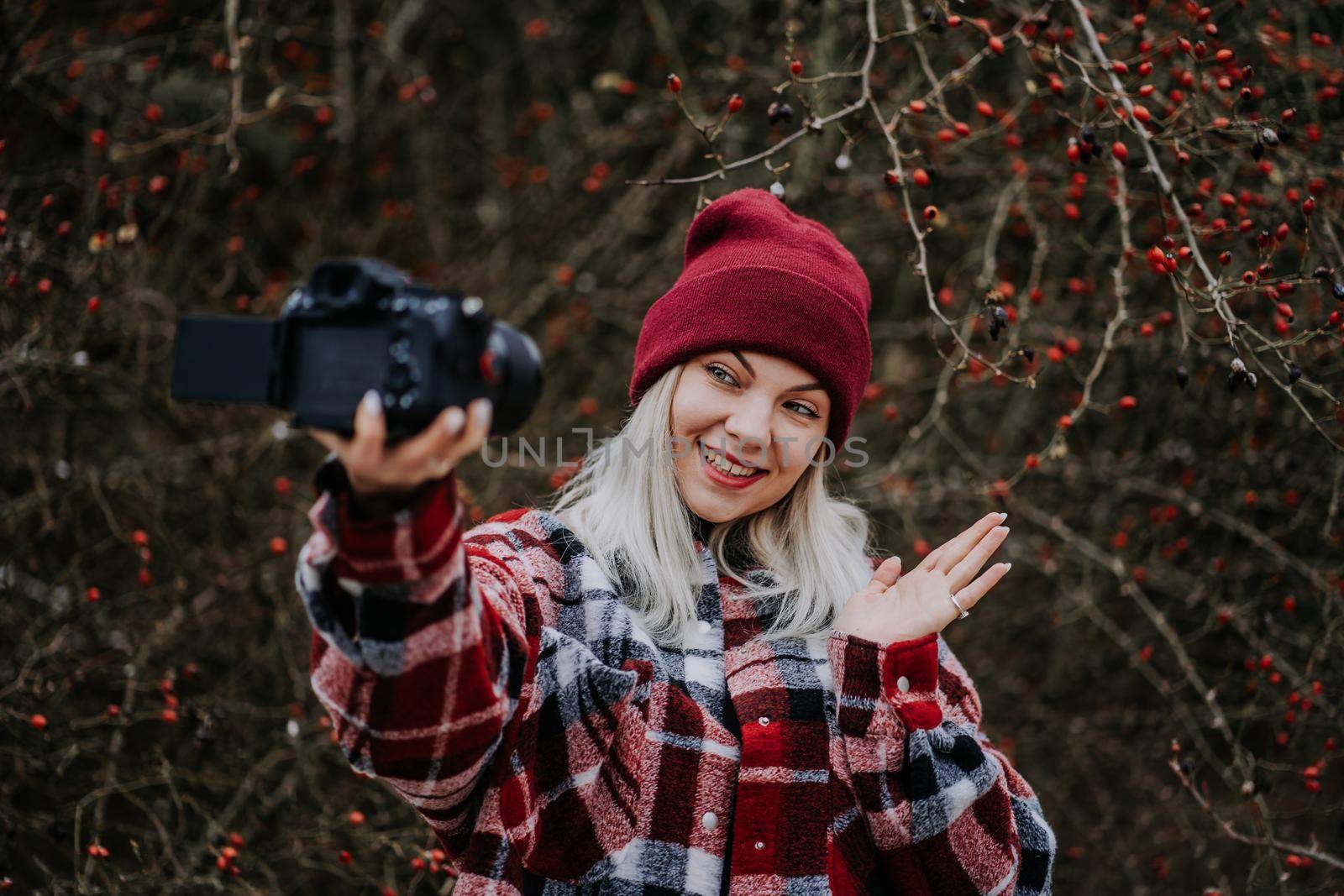 Smiling travel blogger woman making new video blog, vlog, with her camera on nature forest background. Influencer speaking to camera and smiling. High quality photo