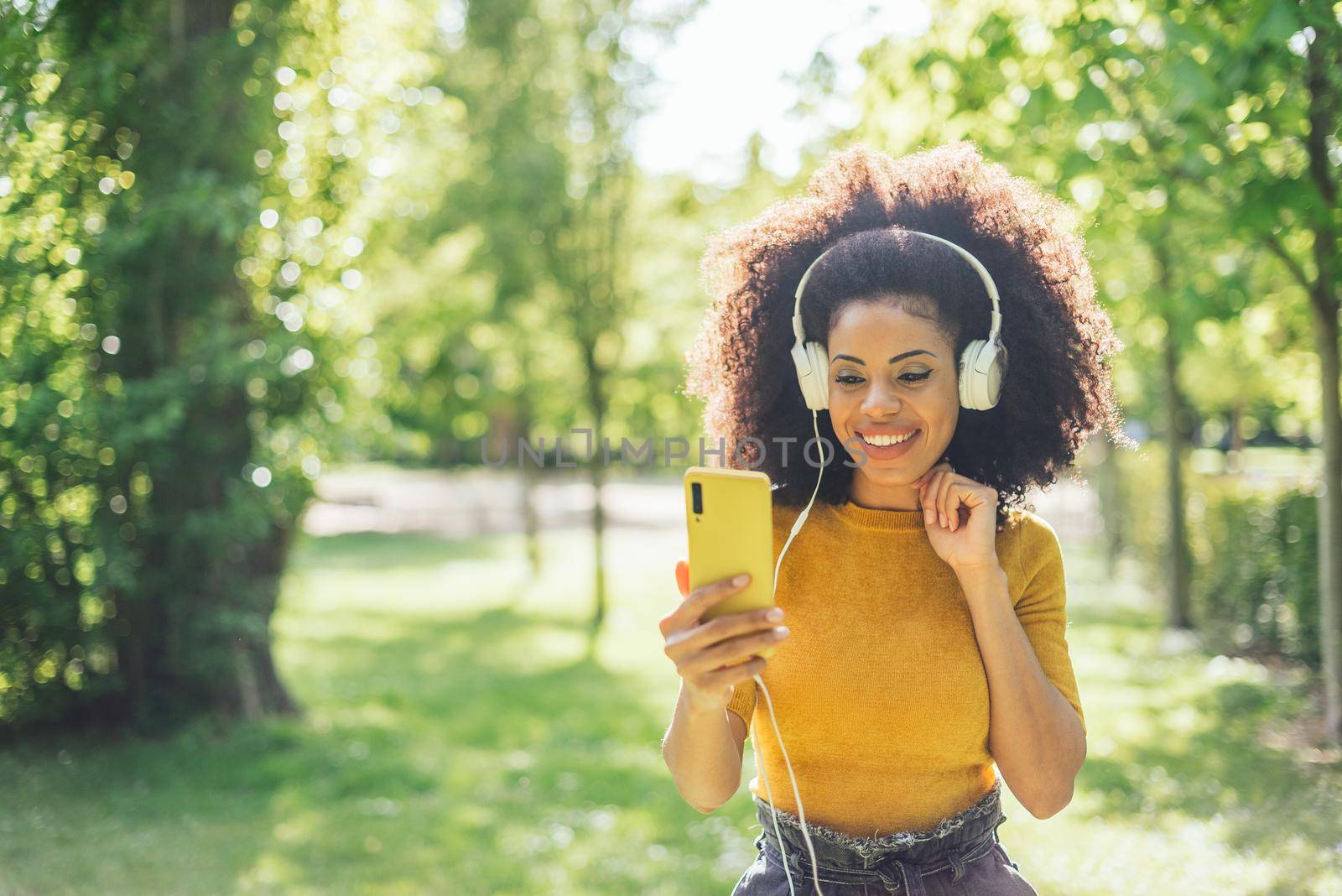 Pretty afro woman listens to music with headphones in a garden. by ivanmoreno