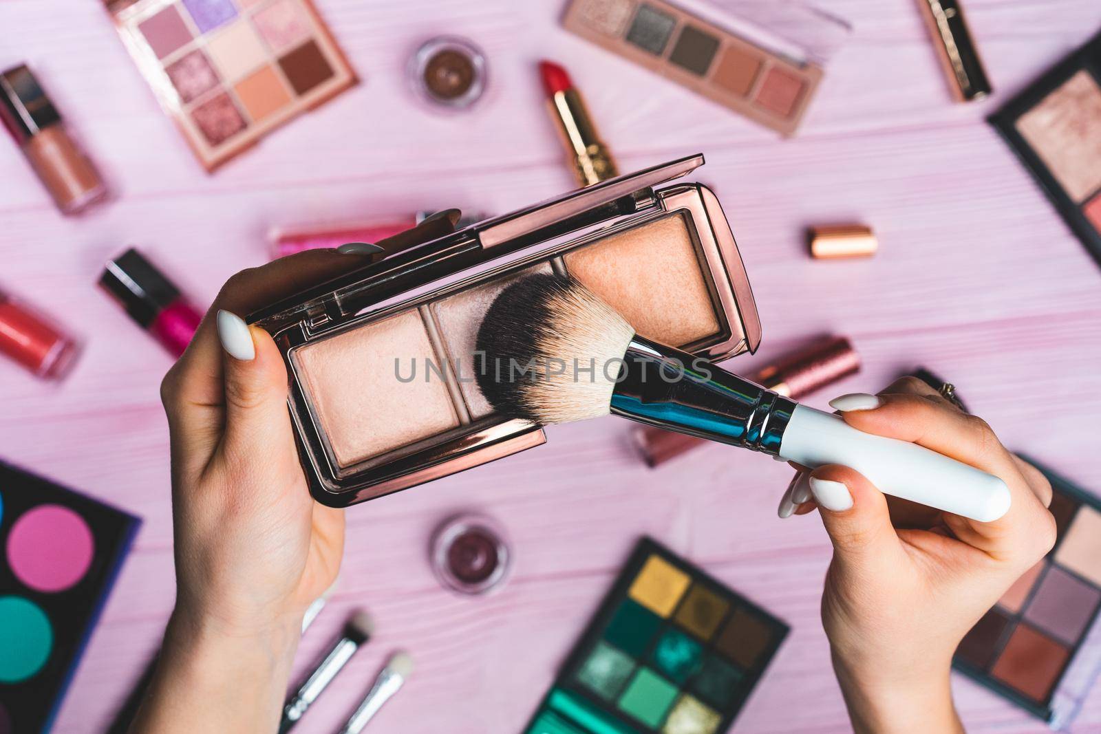 Woman working with face contouring palette - powder, bronzer and highlighter on pink flat lay cosmetics collection background. Tools in beauty industry - lipsticks, eyeshadows, glosses.High quality