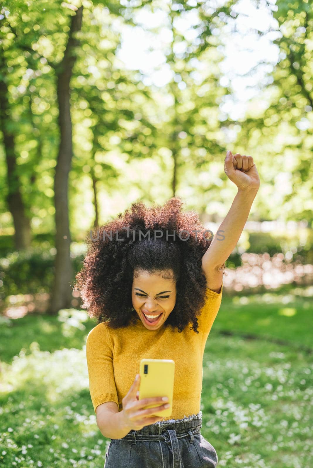 Pretty afro woman chatting on her mobile, celebrating good news. by ivanmoreno