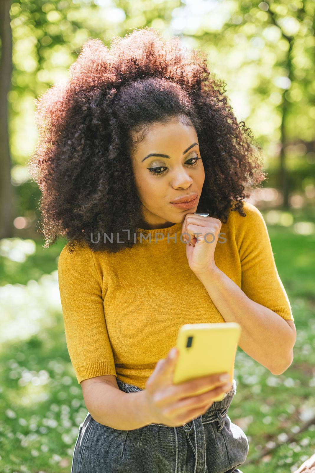 Pretty afro woman chatting surprised, in a park. Selective focus.