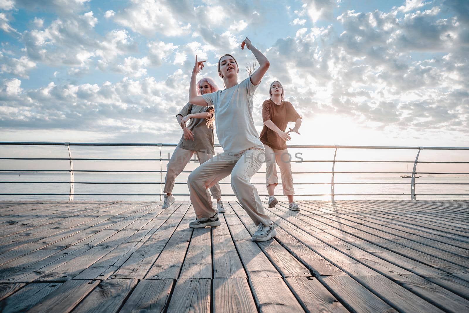 Young dancing teenager girls enjoying funky hip-hop moves. Modern women performing freestyle dance together on sea embankment at sunrise. High quality photo