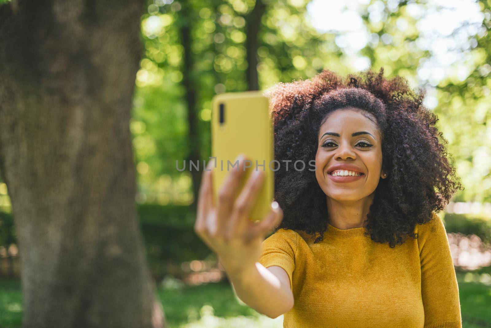 Pretty afro woman taking a selfie smiling in the forest. Selective focus.