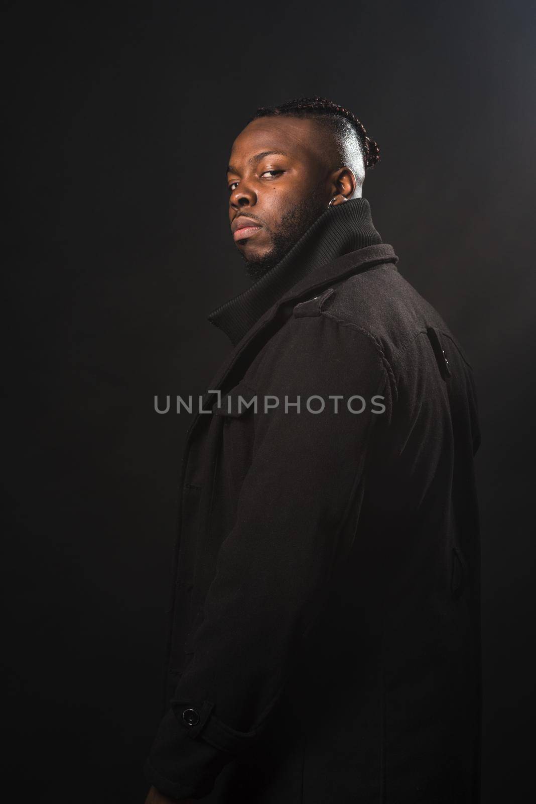 Black man with his back turned to the camera with a serious look. Mid shot. Black background