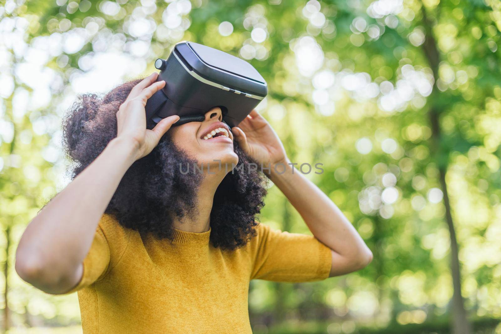 Afro woman wearing a virtual reality glasses in a garden. Selective focus.