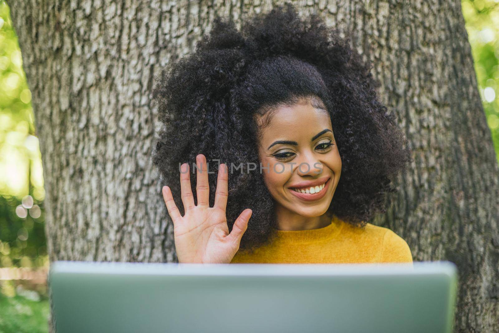 Beautiful and happy afro woman talking on video call with a laptop in a garden. Selective focus.