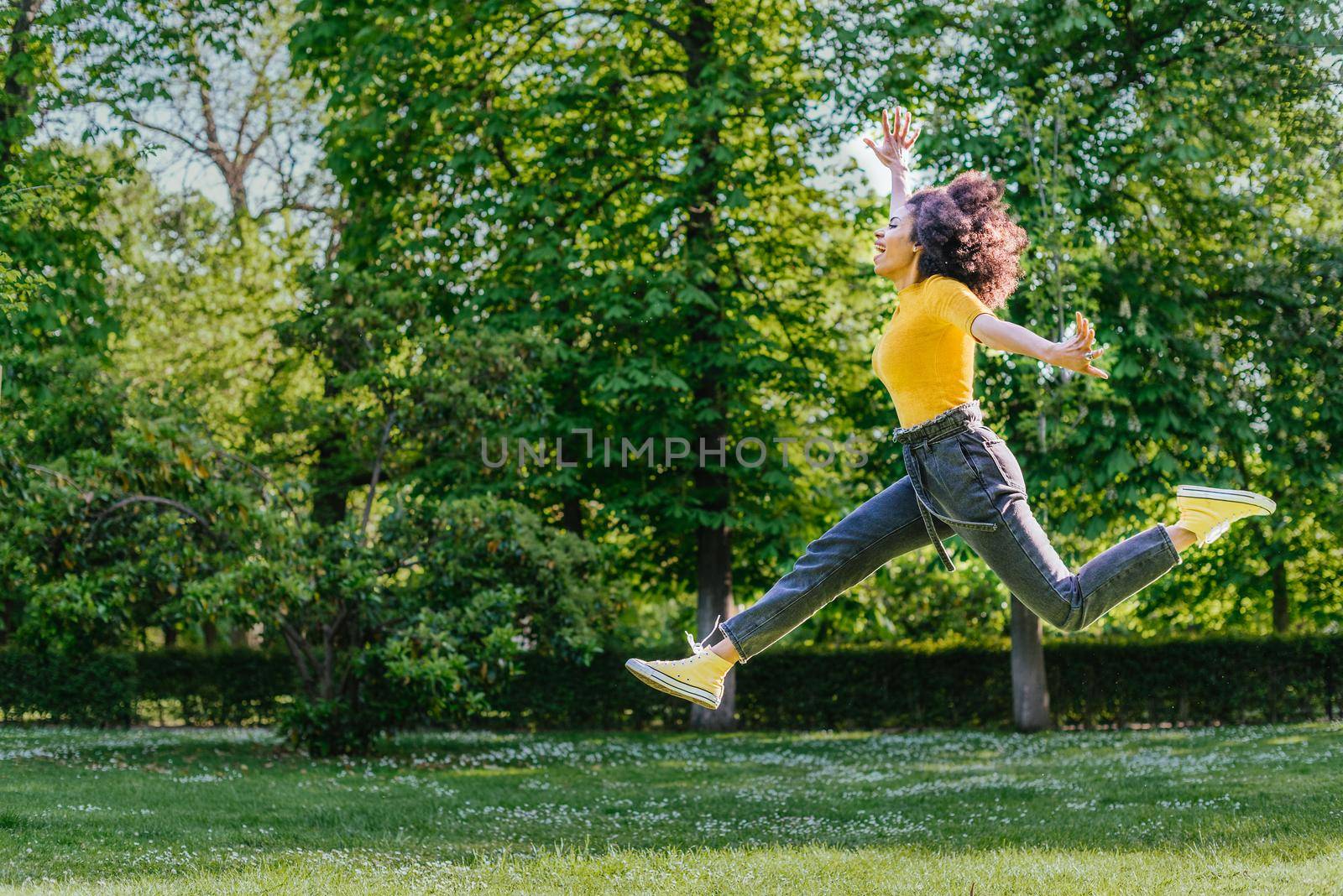 Pretty woman jumping happily in a garden. Side view. Full body.