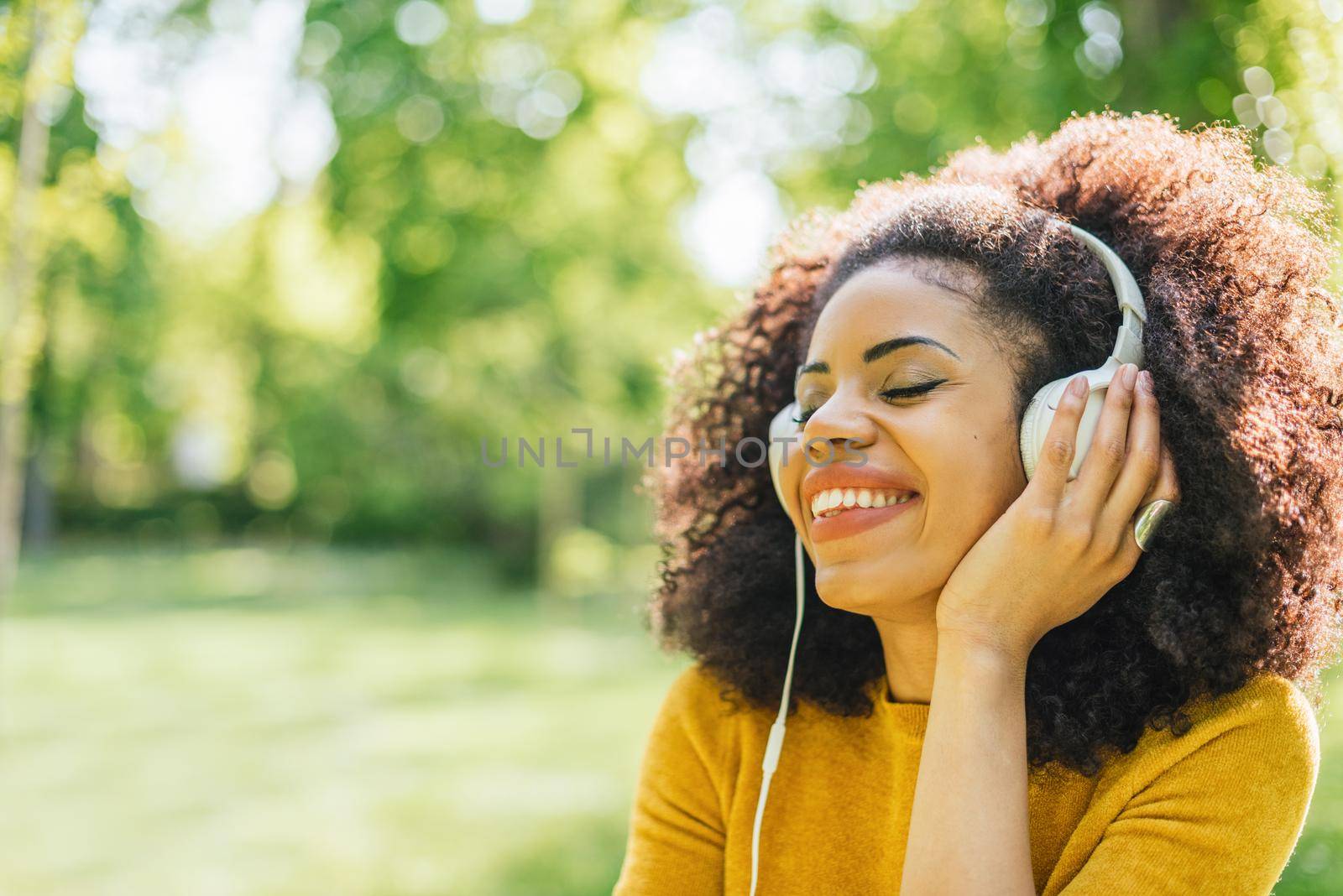 Pretty afro woman listens to music with headphones dancing in a garden. Selective focus.