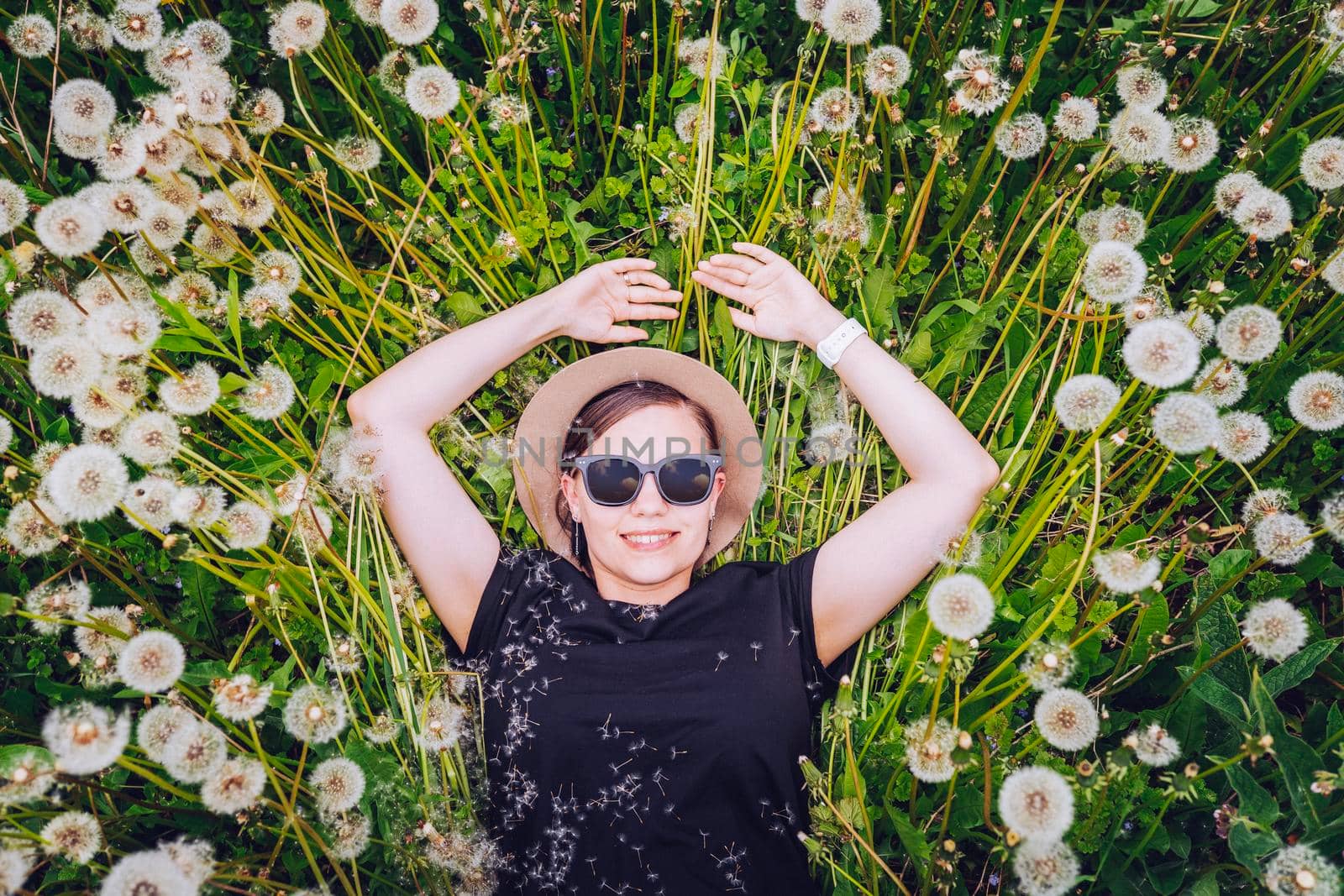Young beautiful girl in sunglasses lies in dandelion field and looks to the sky. Top view. by kristina_kokhanova