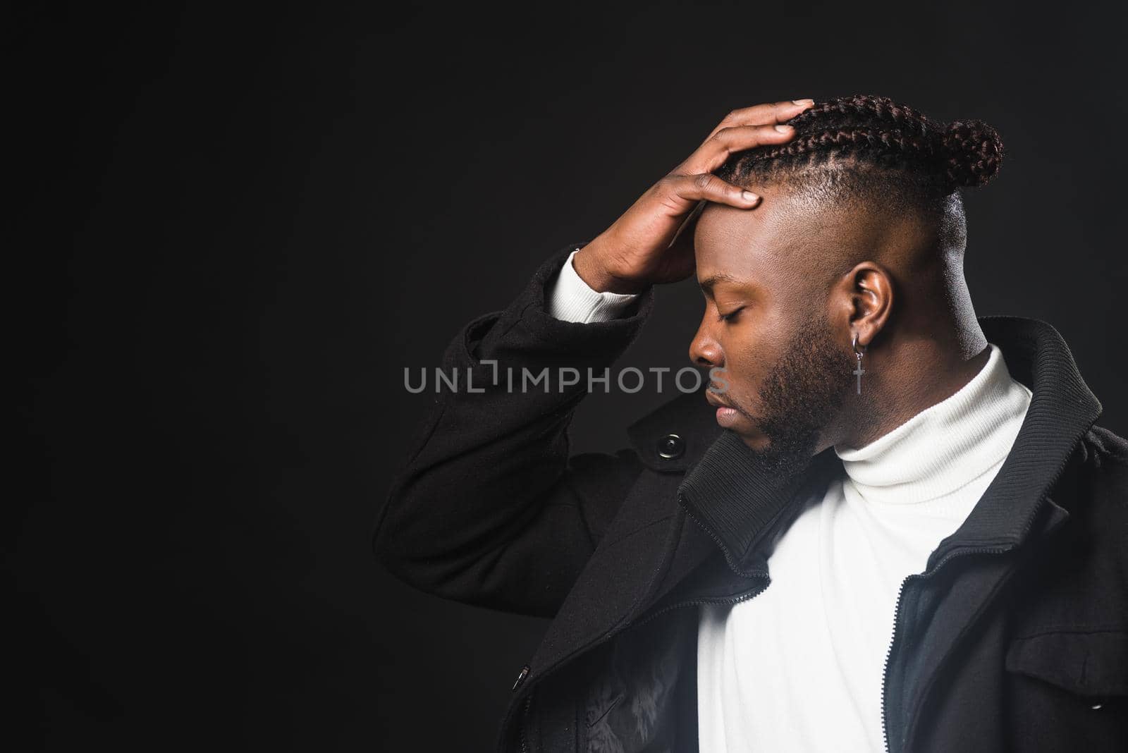 Black man in profile with hand on forehead. Close up. Black background.