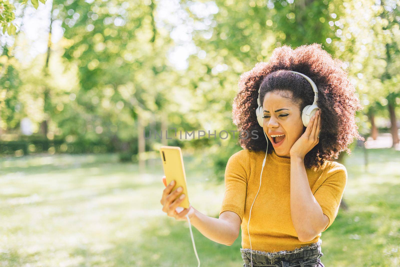 Pretty afro woman listens to music with headphones in a garden. by ivanmoreno