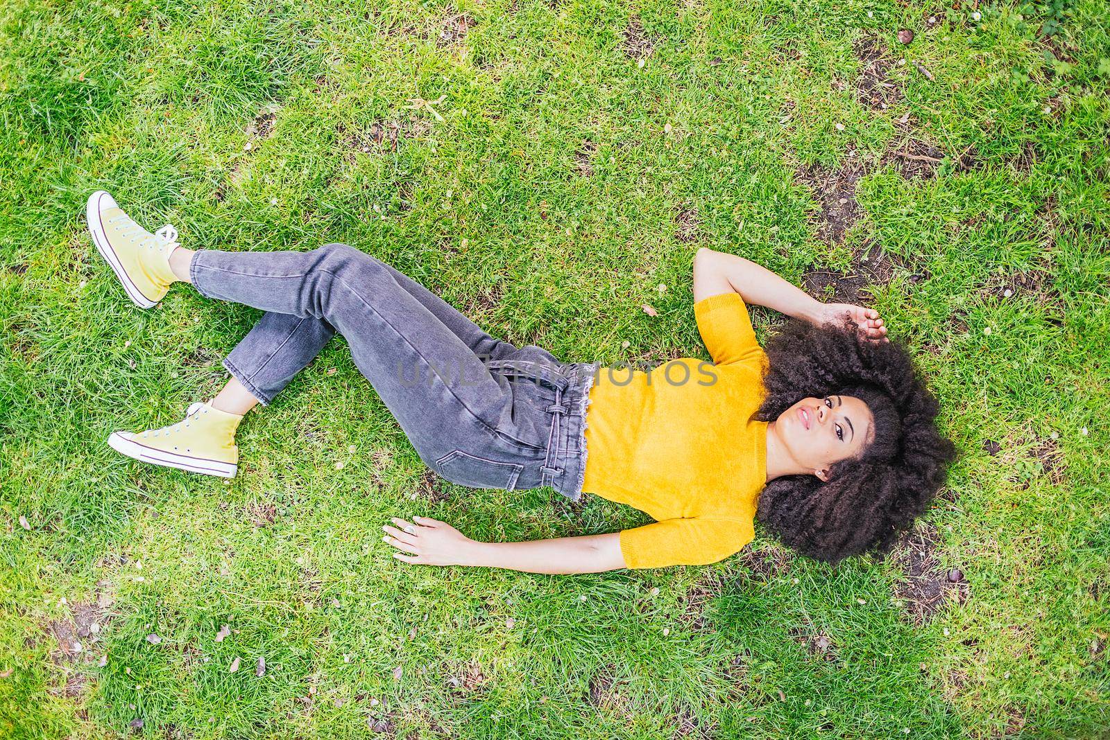 Pretty afro woman lying on her back in a garden. by ivanmoreno