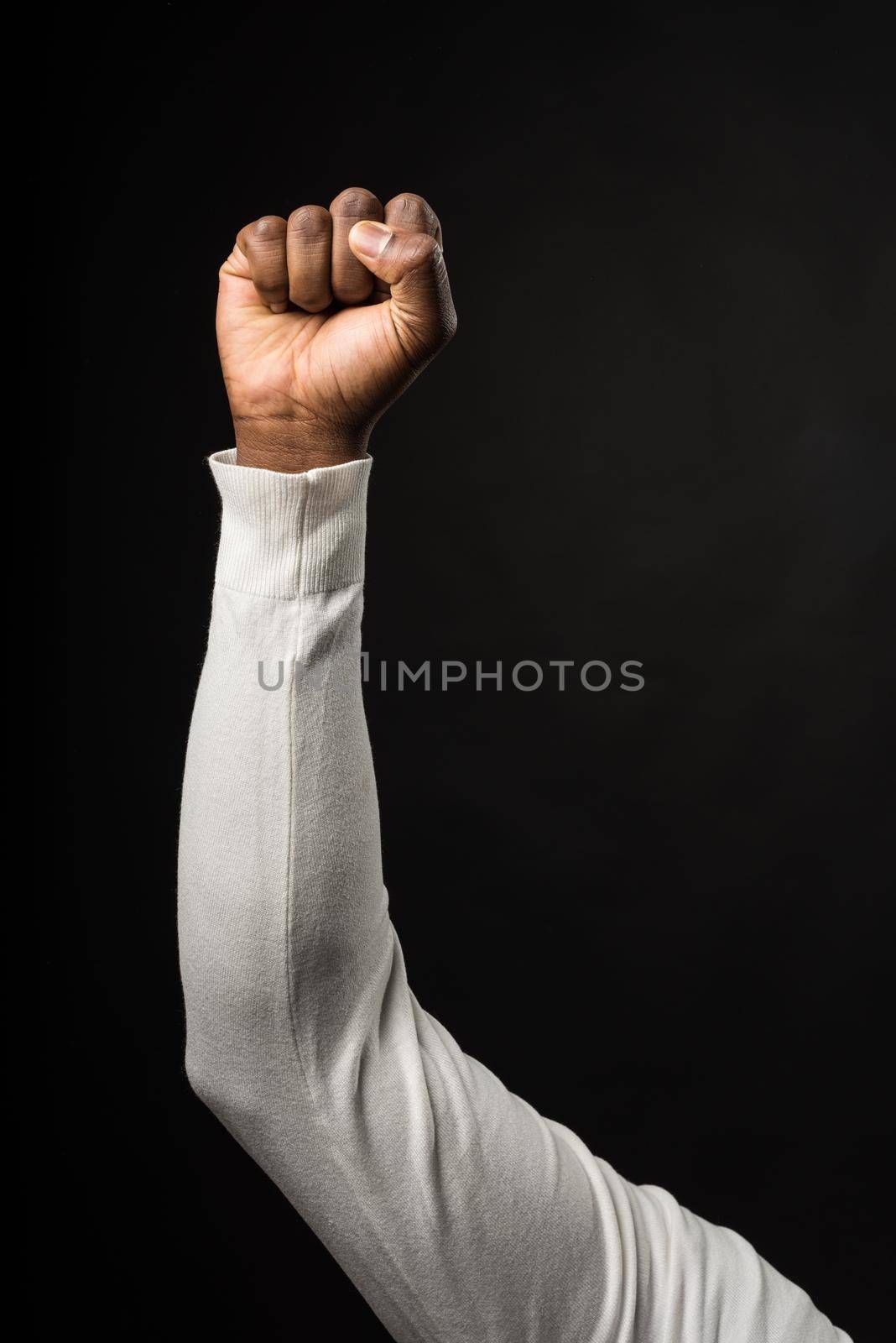 Raised fist of a black man, on a black background, long white sleeves. Close up. Black background.