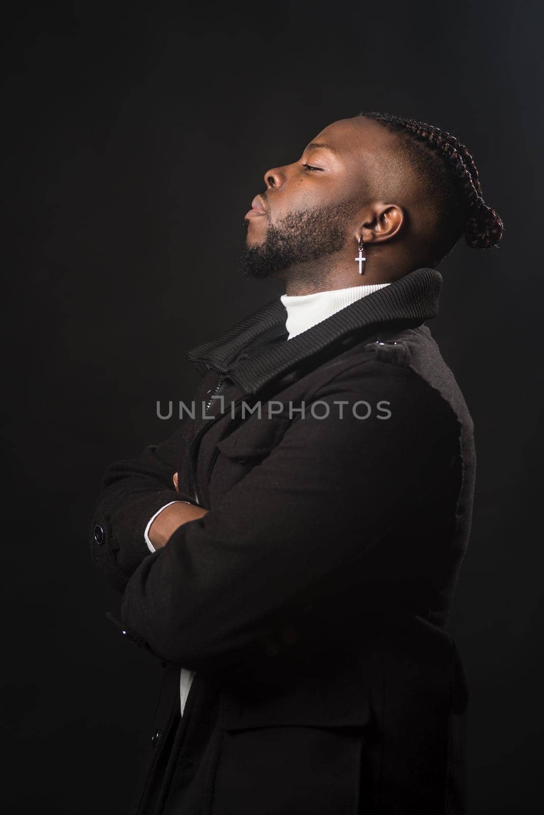 Black man in profile, very serious and with his arms crossed. Mid shot. Black background.