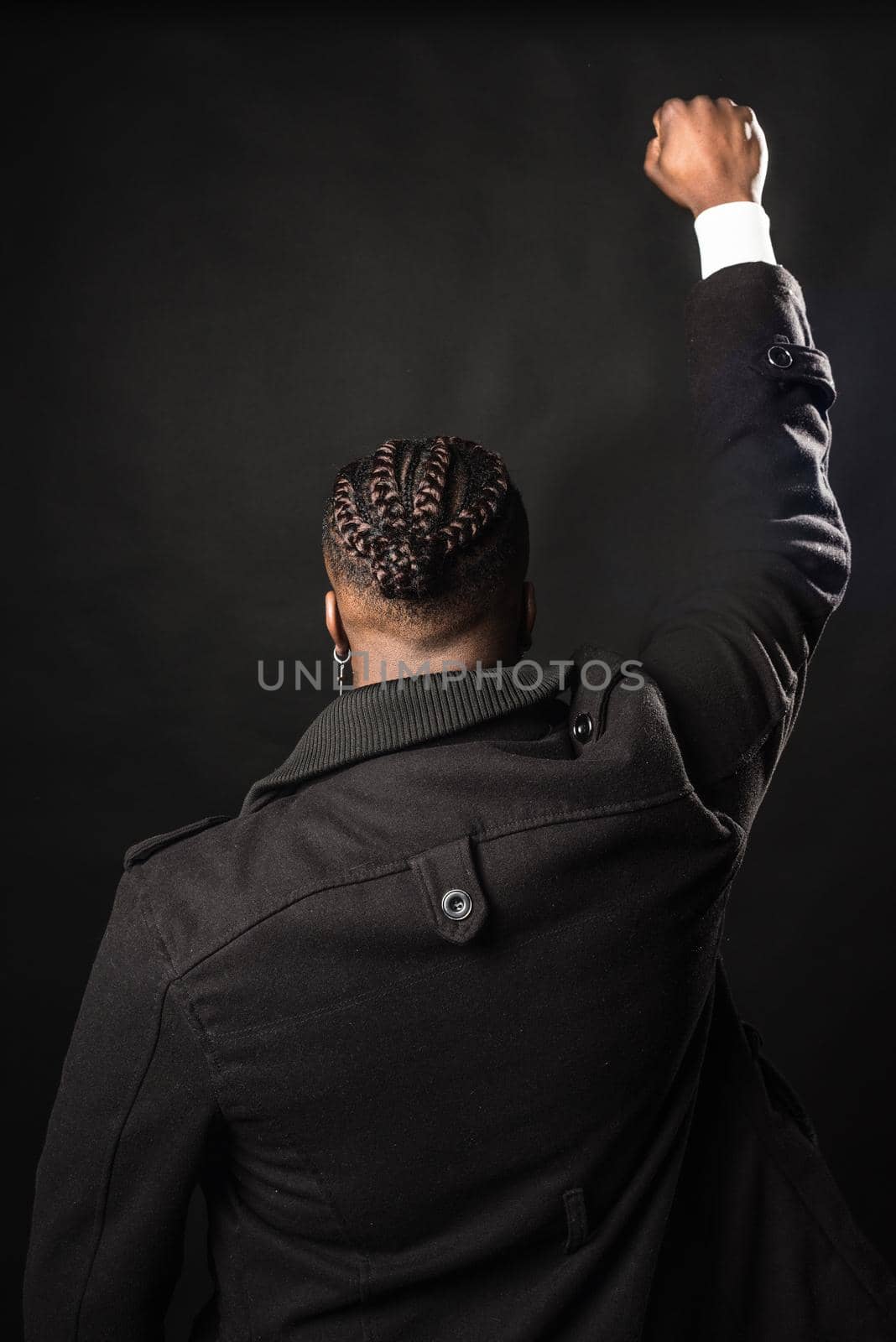 Black man from behind with raised fist. Mid shot. Black background.