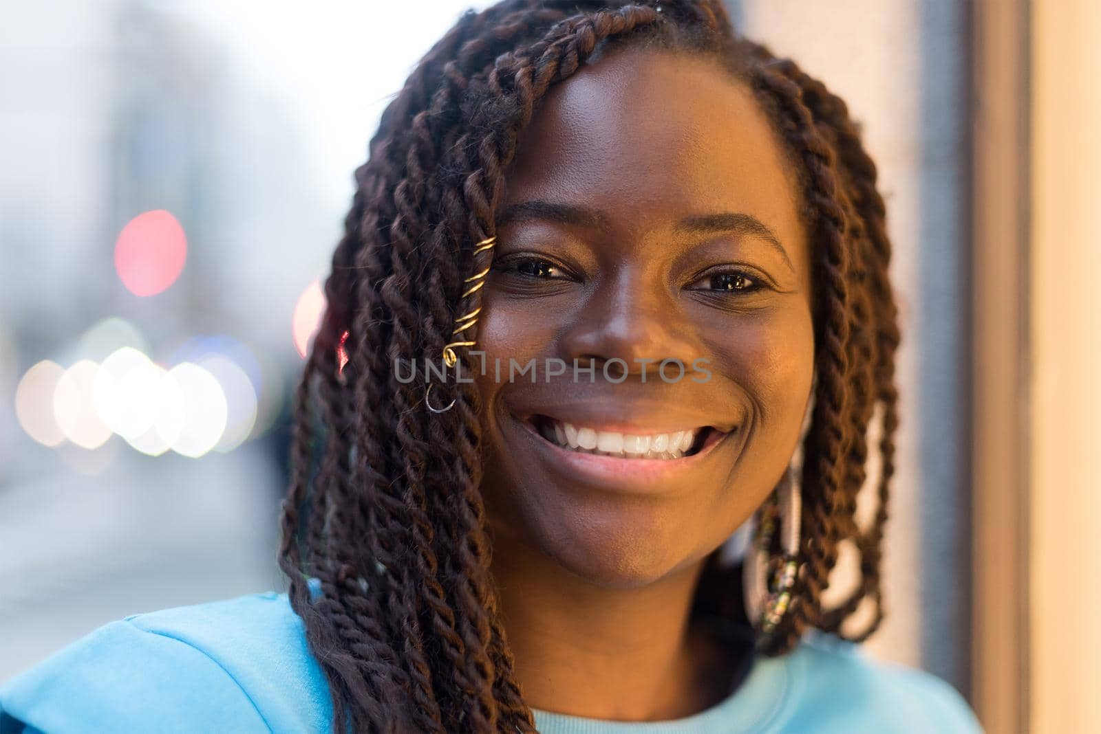 Pretty young black woman in the middle of the city, smiling at camera. Selective focus.
