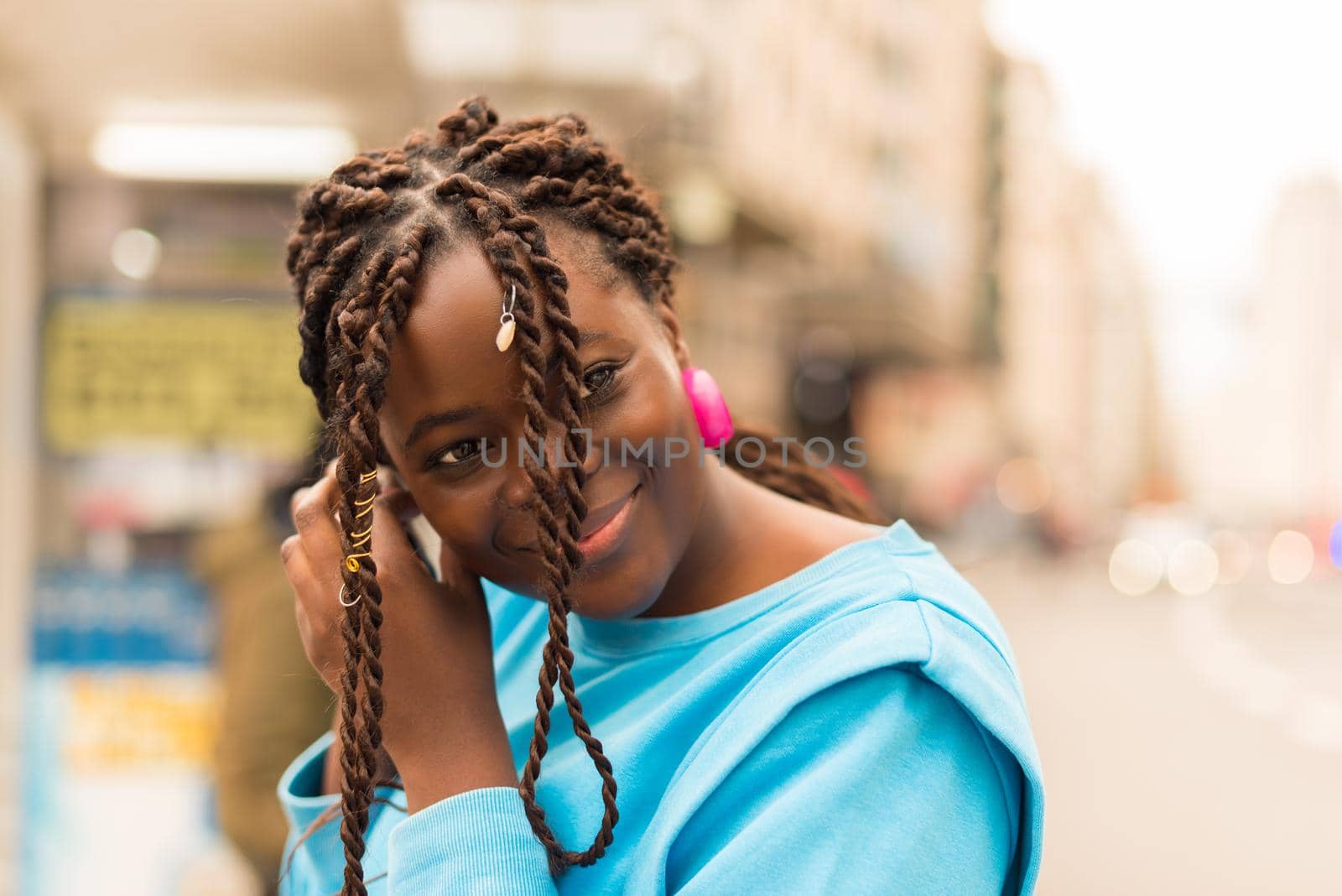 Pretty young black woman putting on her earrings in the middle of the city, smiling. Selective focus.