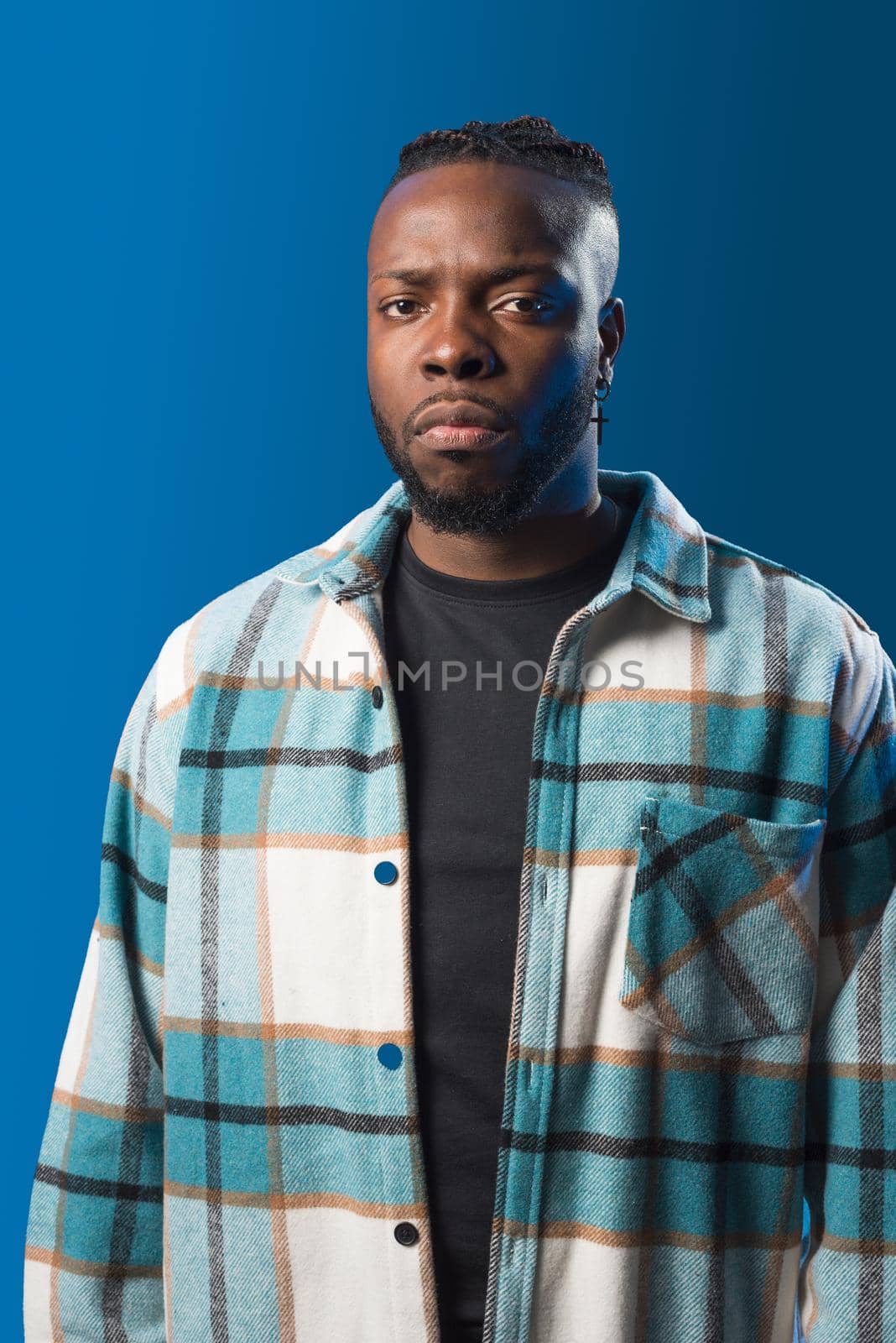 Handsome black man looking at mobile, serious and angry. Mid shot. Blue background.