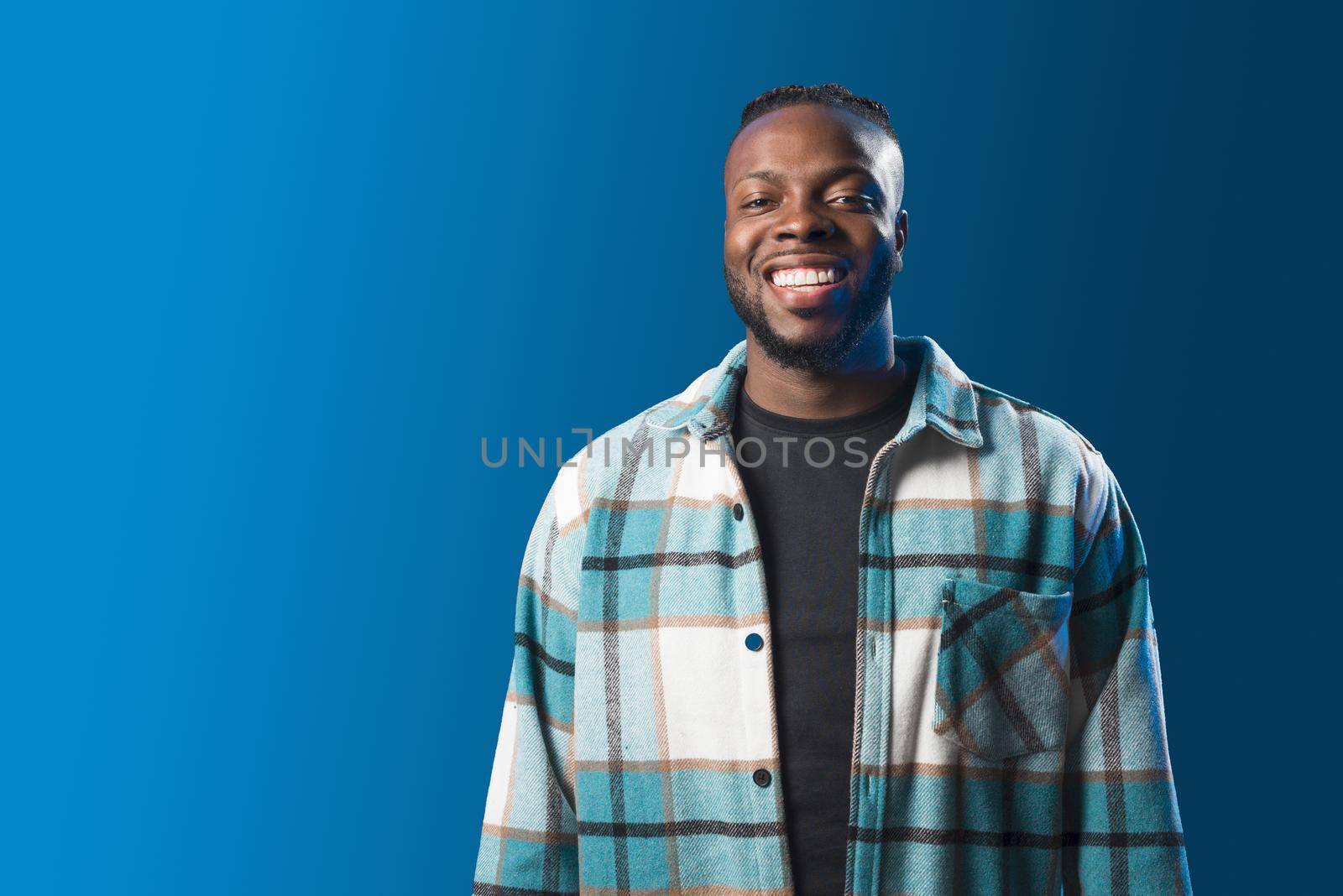 Handsome black man smiling in confident pose. Mid shot. Blue background