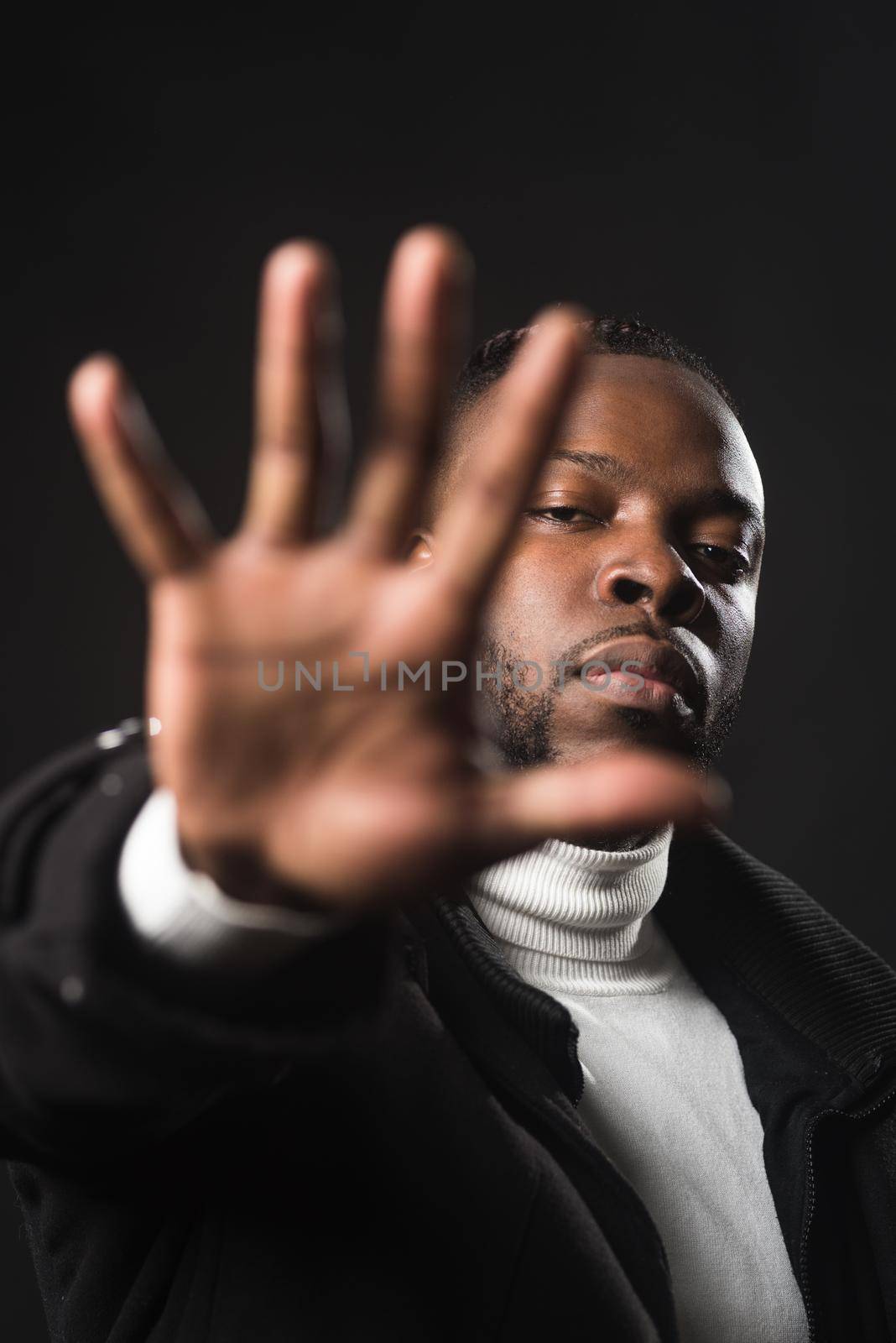 Serious black man telling you to stop with an open hand. Close up. Black background.