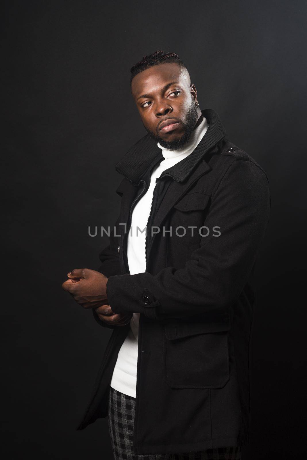 Handsome black man posing, putting on his jacket sleeve. Mid shot. Black background.