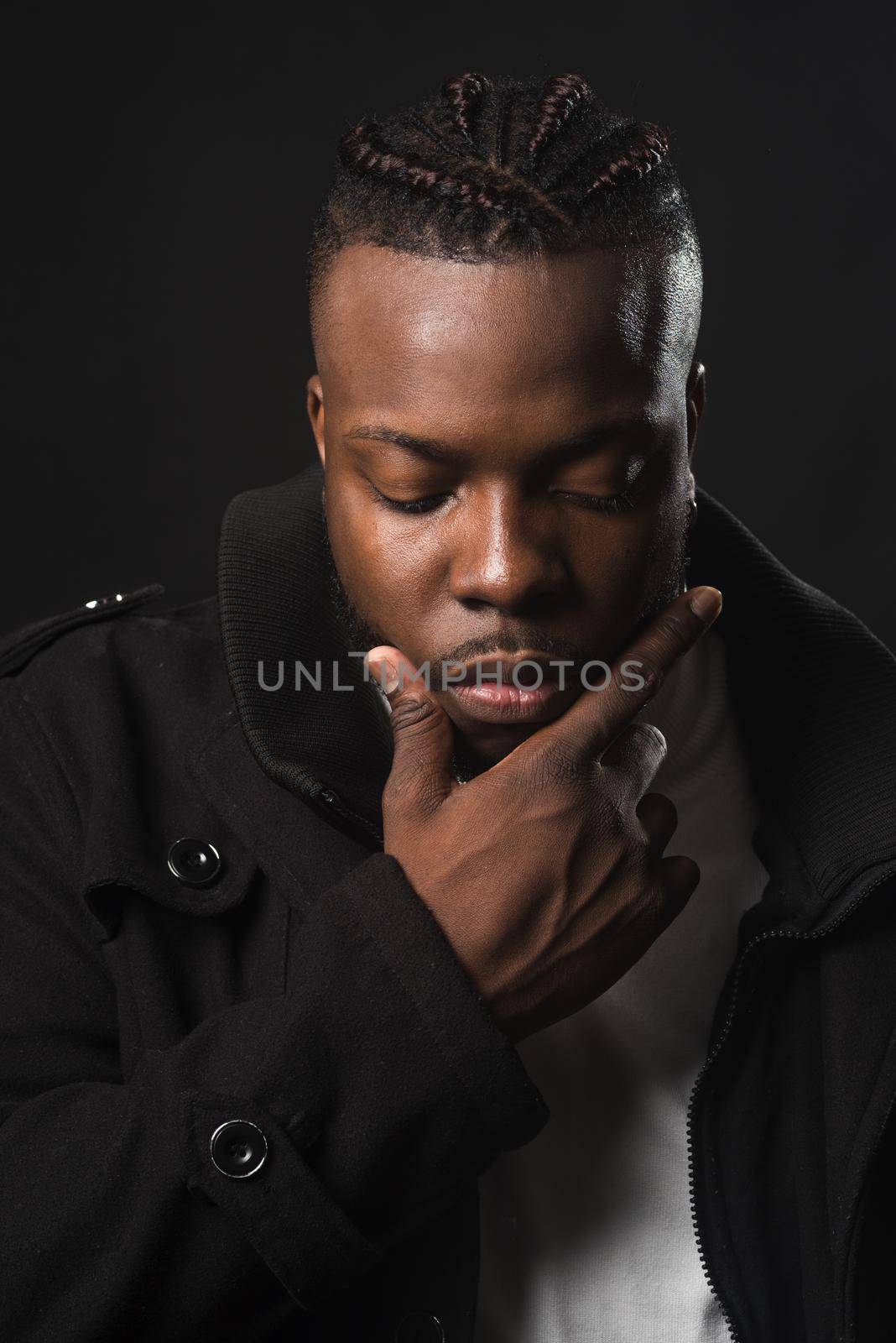 Handsome black man touching his chin in a pensive pose, looking down. Close up. Black background.