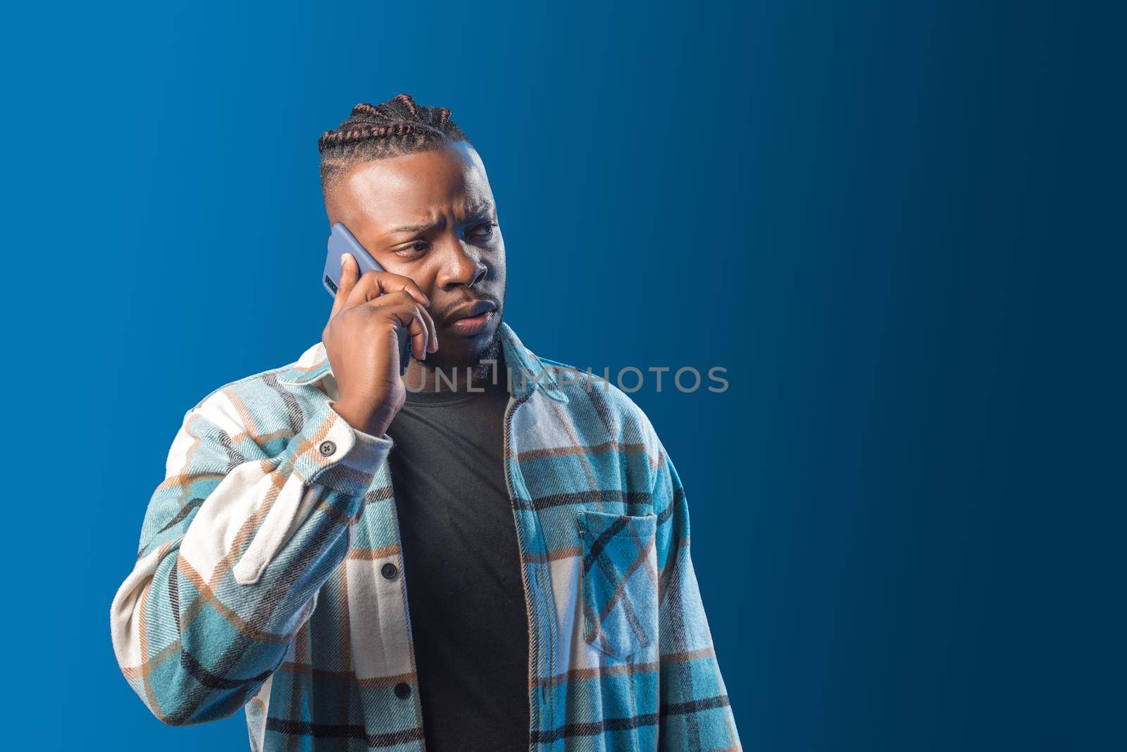 Handsome black man talking on the mobile worried. Mid shot. Blue background.