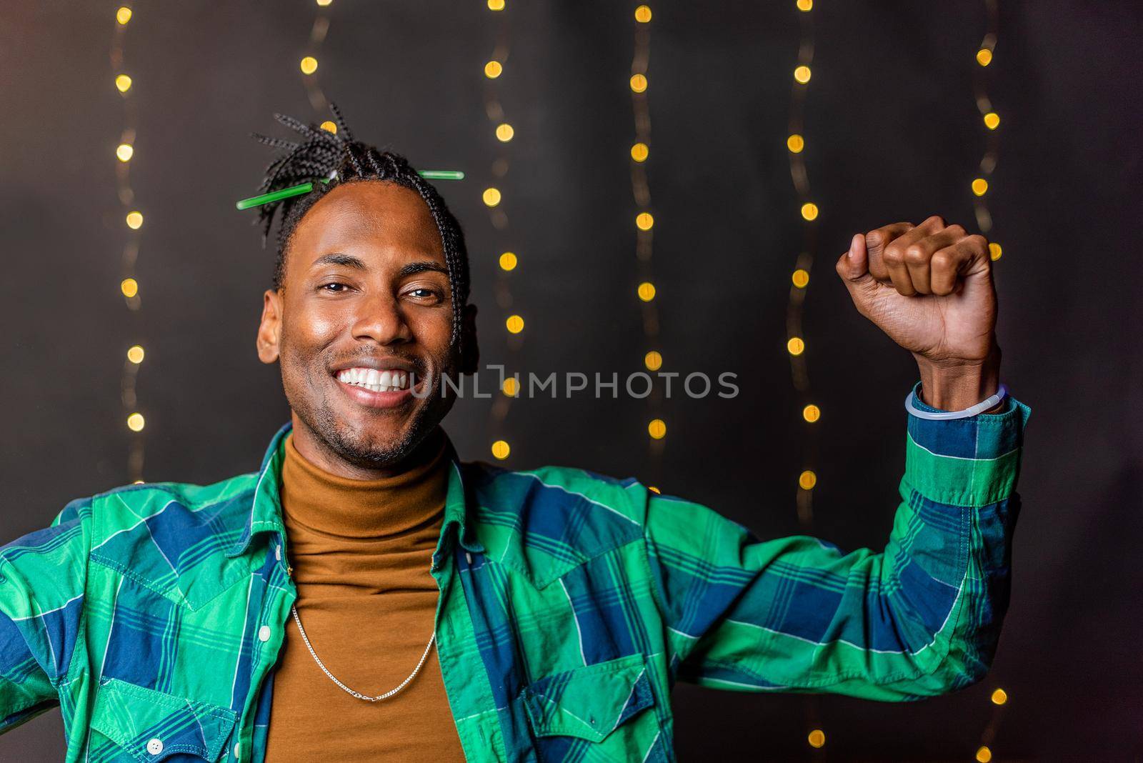 Portrait of a cheerful young African American with braids with clenched fists looking at the camera on a blurred light background.