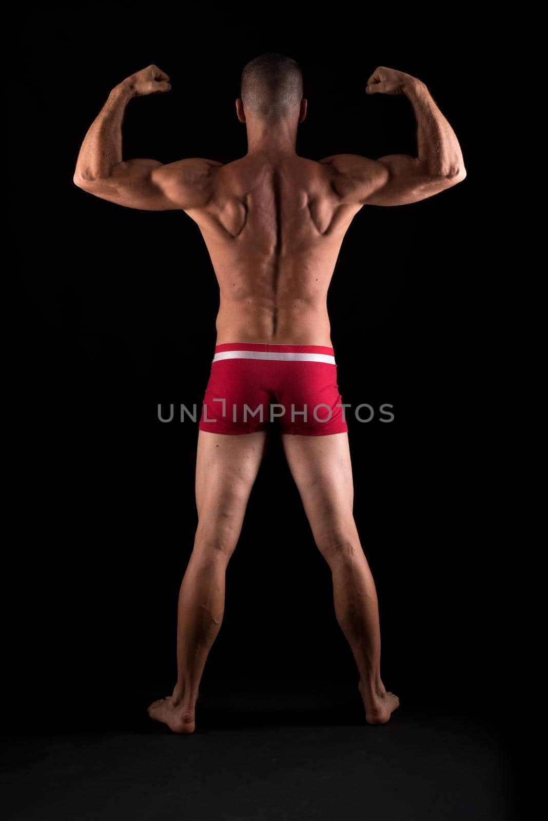 Athletic man in underwear. Full body, back. Black background.