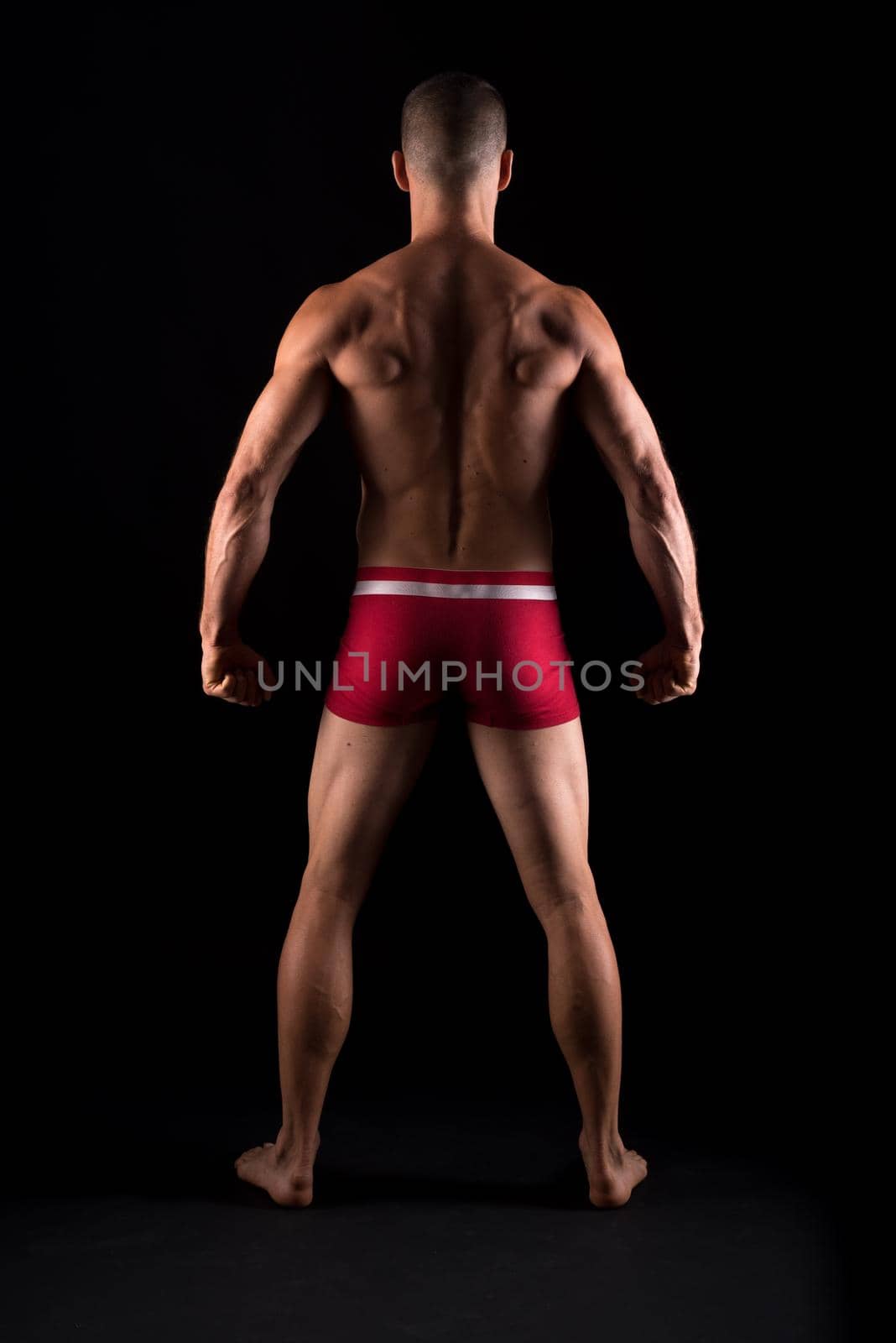 Athletic man in underwear. Full body, back. Black background.