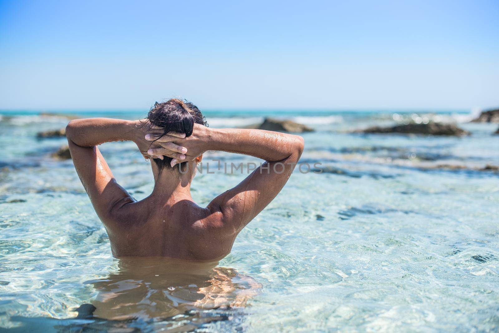 Woman bathing in a heavenly sea of turquoise water. With his back to the camera, looking at the horizon. Mid shot. Formentera island. Spain.