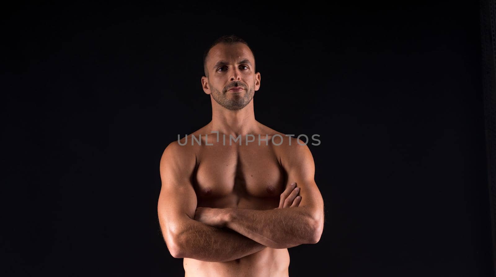 Athletic man without shirt. Mid shot. Black background.