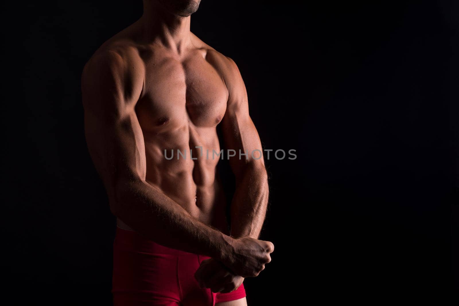 Muscular trunk of man in tension. Mid shot. Black background.