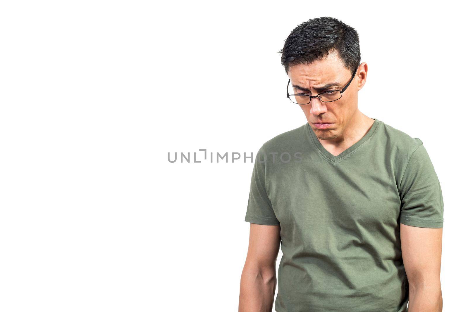 Sad man in green t shirt and glasses pouting lips and looking down while feeling depressed against white background