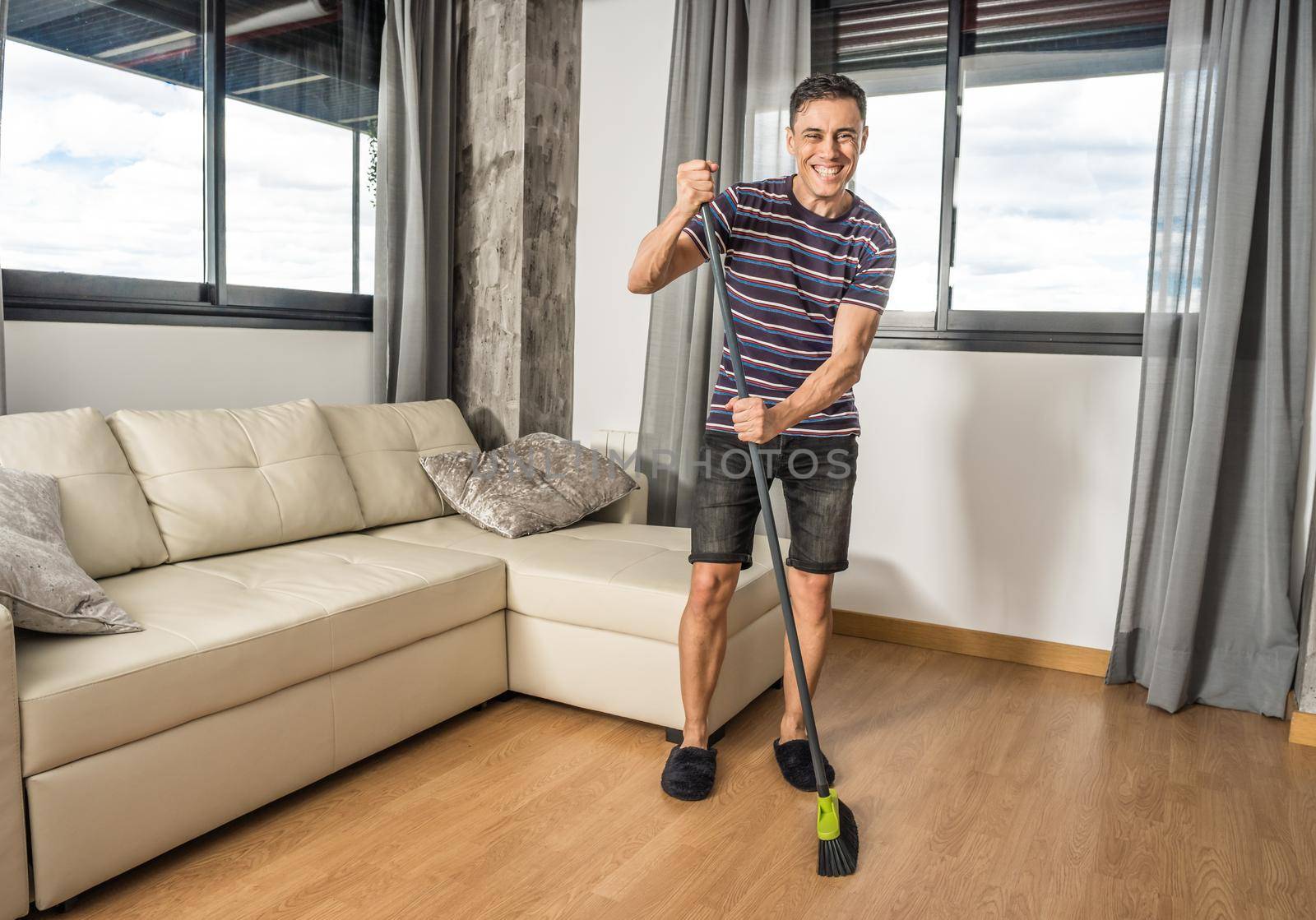 Smiling man in casual clothes and slippers sweeping his living room. Full body.