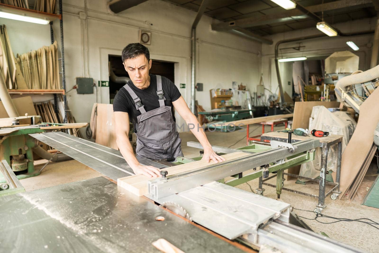 Worker cutting on a sliding table saw in a factory. Mid shot.