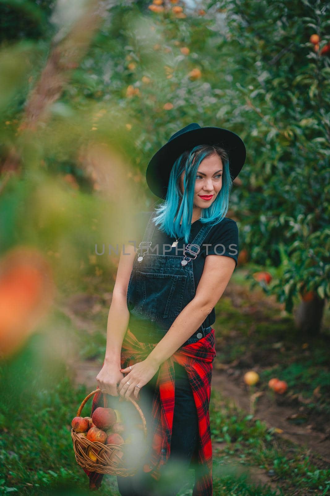 Pretty unusual woman with blue dyed hair walking alone between trees in apple garden at autumn season. Girl goes ahead away from camera. Organic, nature concept by kristina_kokhanova