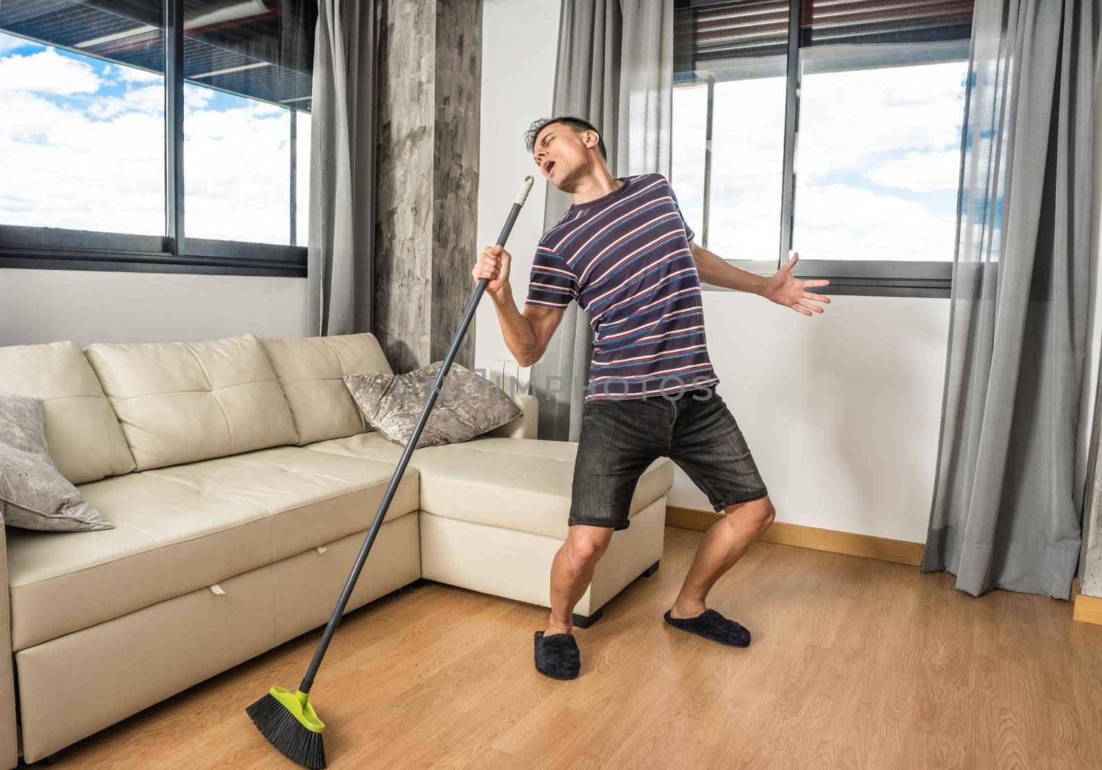 Man singing in the living room of his house holding the broom as if it were a microphone. Full body.
