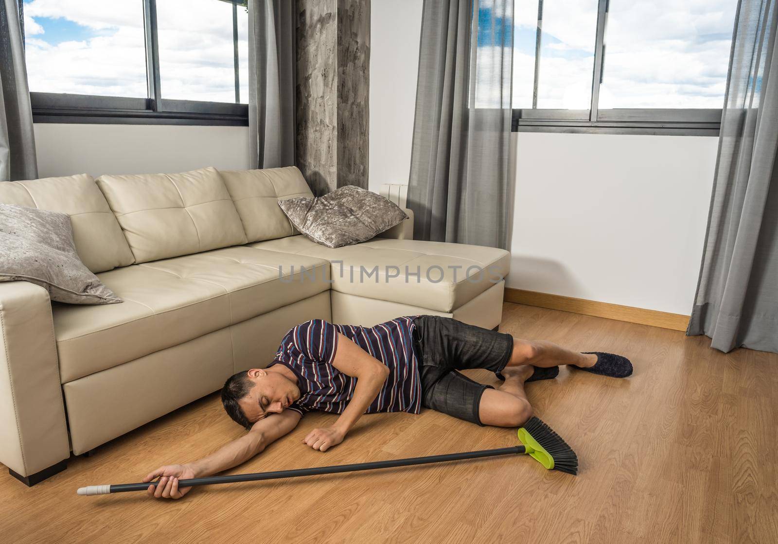 Man who was sweeping the living room of his house and fell asleep on the floor. Full body.