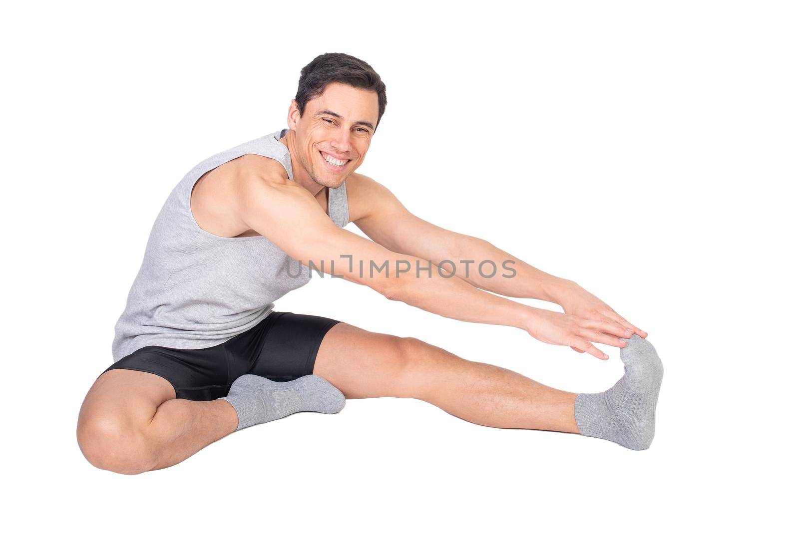 Full body of positive sportive male in sportswear looking at camera with smile while stretching femoral muscle isolated on white background